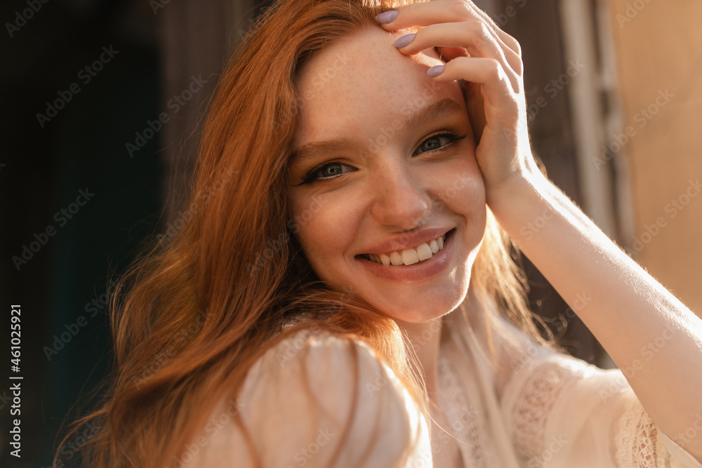 Close-up face of blue-eyed young european girl with red hair. Delicate refined hand at temple with lilac lacquer. Smile on her face is wide and beautiful. Vacation, happiness and pleasure concept Close-up face of blue-eyed young european girl with red hair. Delicate refined hand at temple with lilac lacquer. Smile on her face is wide and beautiful. Vacation, happiness and pleasure concept