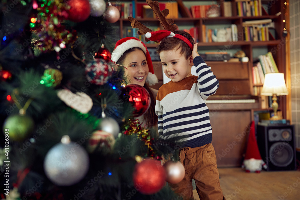Happy little boy decorates Christmas tree with his mother at home. Happy little boy decorates Christmas tree with his mother at home.