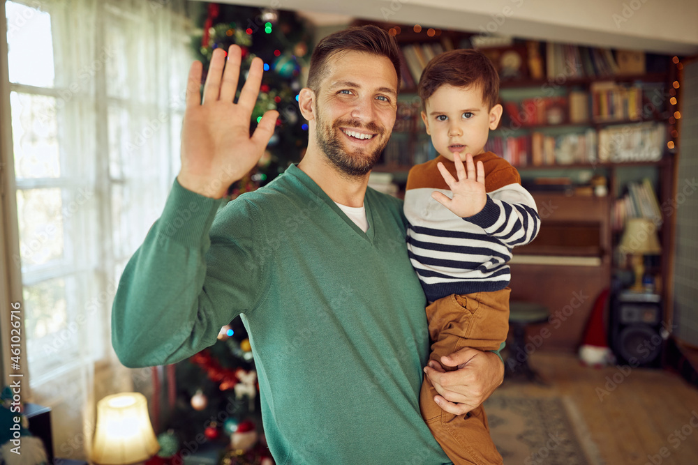 Happy father and son wave to camera while celebrating Christmas at home.