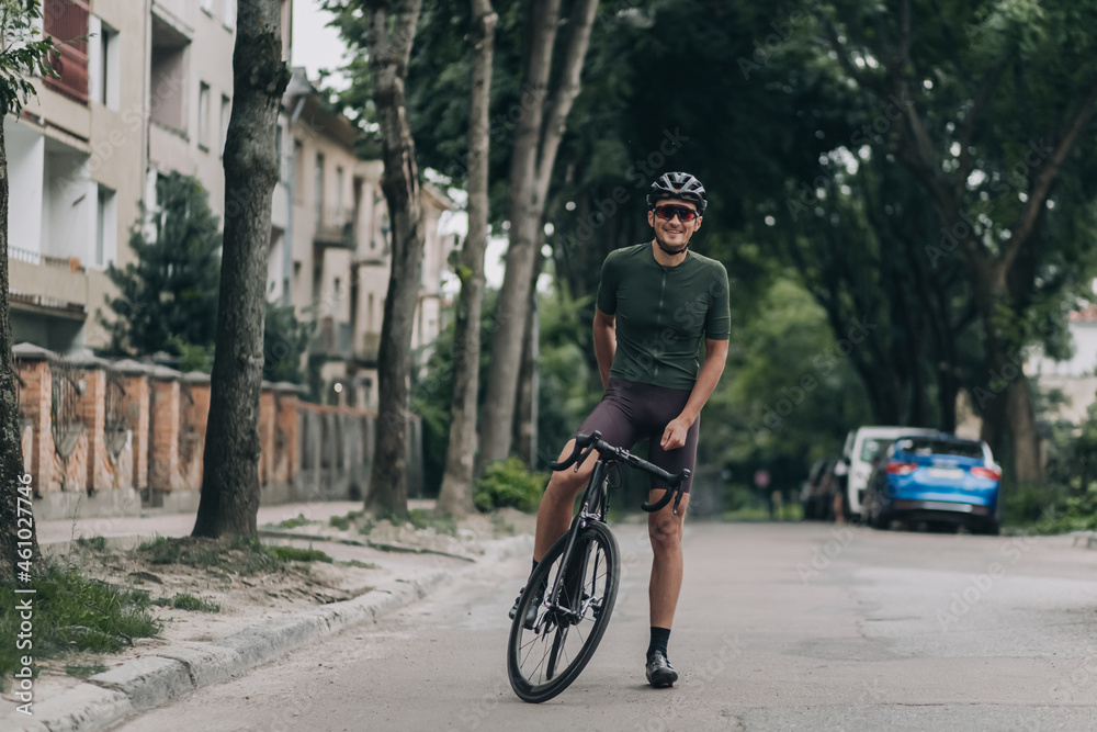 Fototapeta premium Positive cyclist with bike resting on street after ride