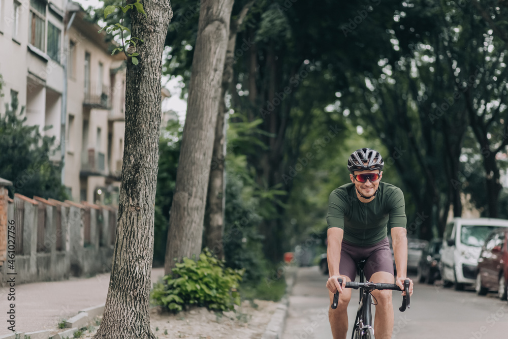 Fototapeta premium Smiling man riding bike in safety helmet along city street