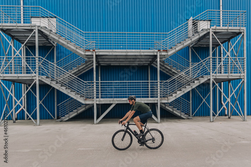 Active man in sportswear riding bike outdoors over blue wall