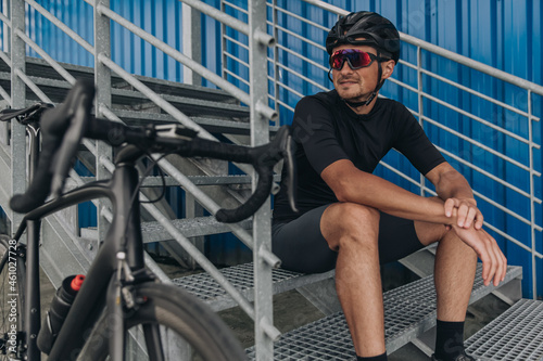 Cyclist sitting on metal stairs near his bike outdoors