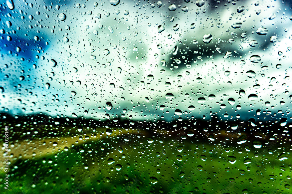 Raindrops on the window in the rainy day. Summer. Rain. Green field in the background. Raindrops on the window in the rainy day. Summer. Rain. Green field in the background.