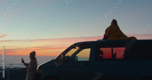 Two friends enjoy a beautiful pink sunset from top of mountain near camper van. Concept vanlife outdoor lifestyle. Cinematic roadtrip, weekend getaway and camping vibes