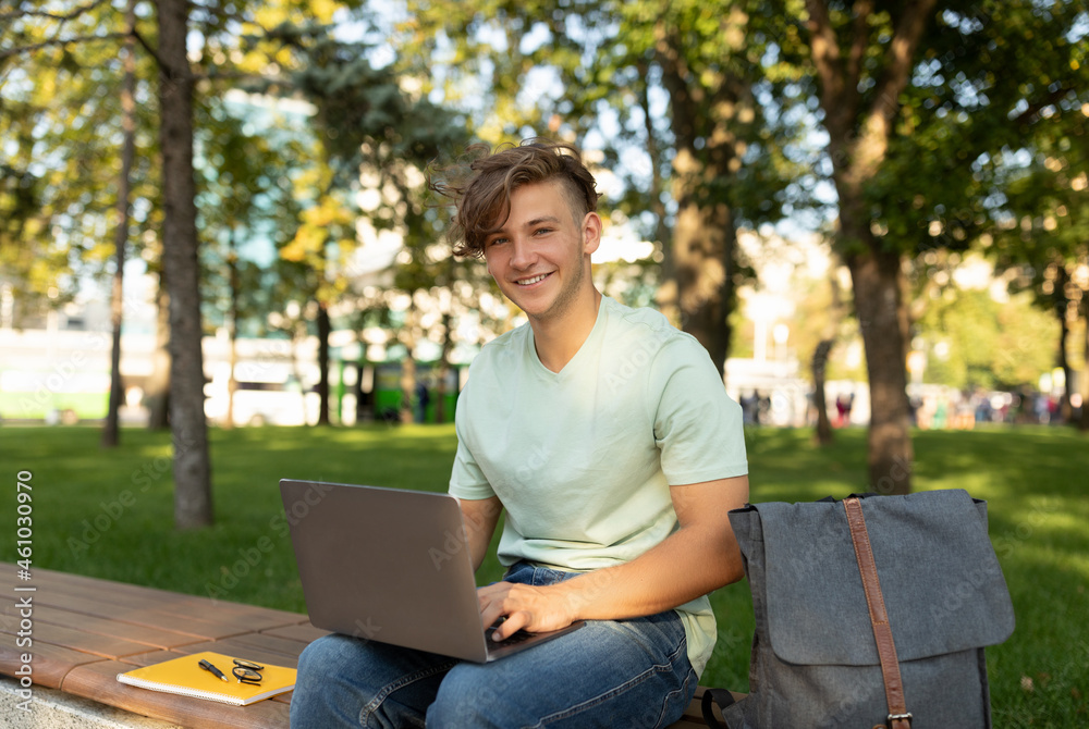 E-learning. Excited male student with laptop attending online lecture, sitting on bench in park outdoors E-learning. Excited male student with laptop attending online lecture, sitting on bench in park outdoors