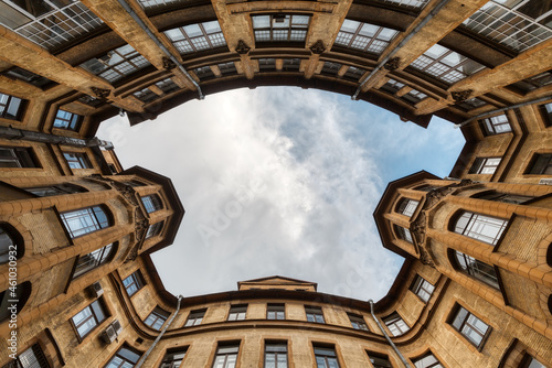 Photo of symmetrical courtyard in residential house from historical center of Saint Petersburg in Russia. Blue cloudy sky. The facade with two bay windows is decorated with sculptures of gargoyles.