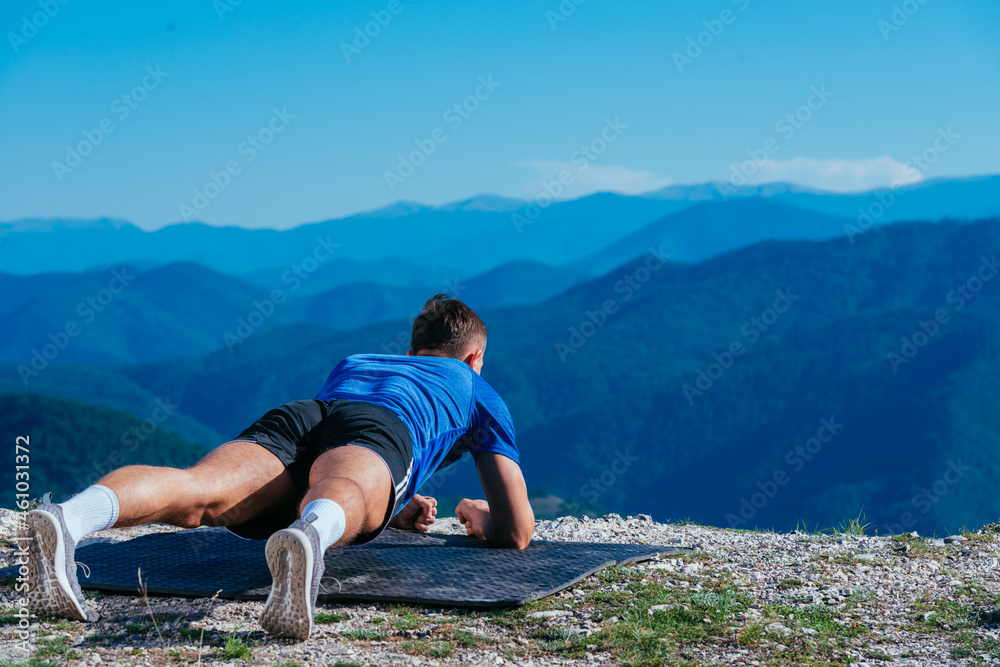 Naklejka premium Strong male athlete doing plank while exercising his abs on top of a mountain on a sunny day.