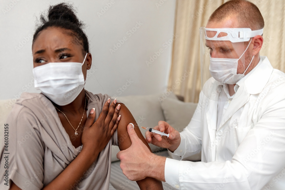 Vaccination against covid-19 epidemic, health protection procedure and immunization. Millennial Caucasian doctor in protective mask gives injection with syringe to nervous patient in clinic.