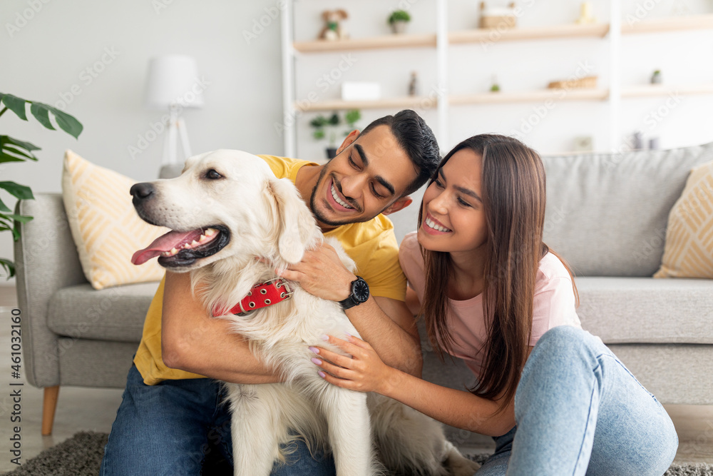 Portrait of happy multiracial couple scratching their pet dog, sitting on floor at home Portrait of happy multiracial couple scratching their pet dog, sitting on floor at home