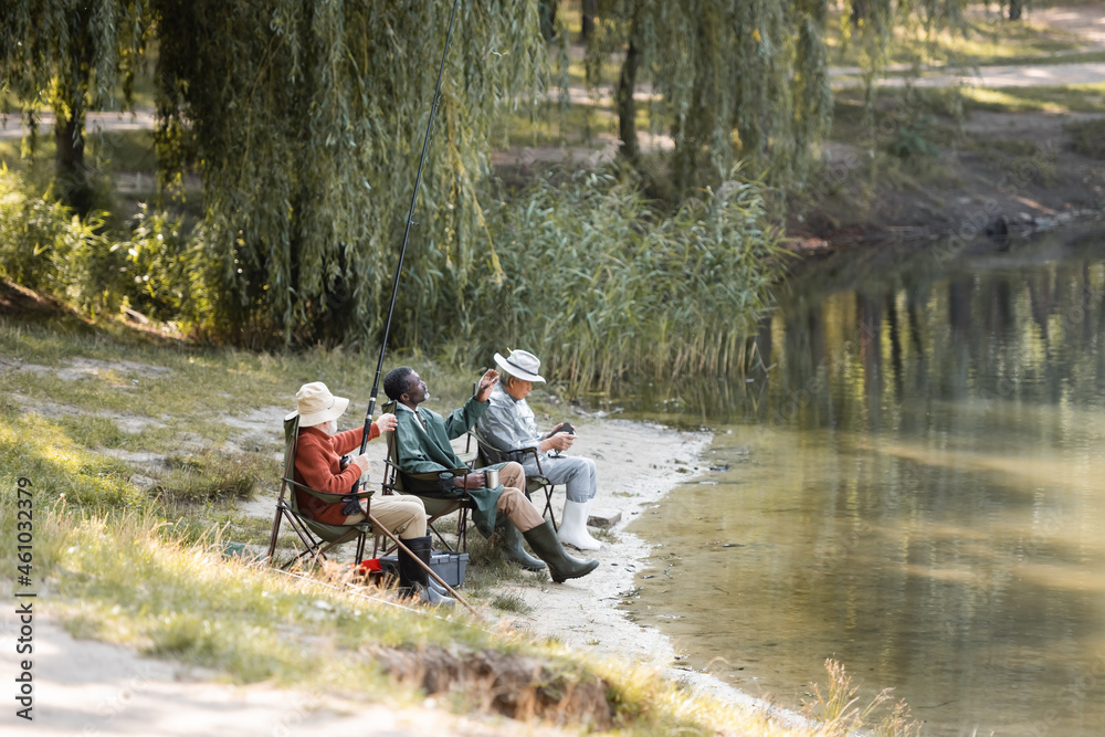 Multiethnic senior men with fishing rod sitting near lake in park