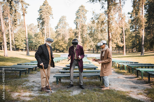 Multiethnic senior friends with smartphone and walking cane using vr headsets in autumn park