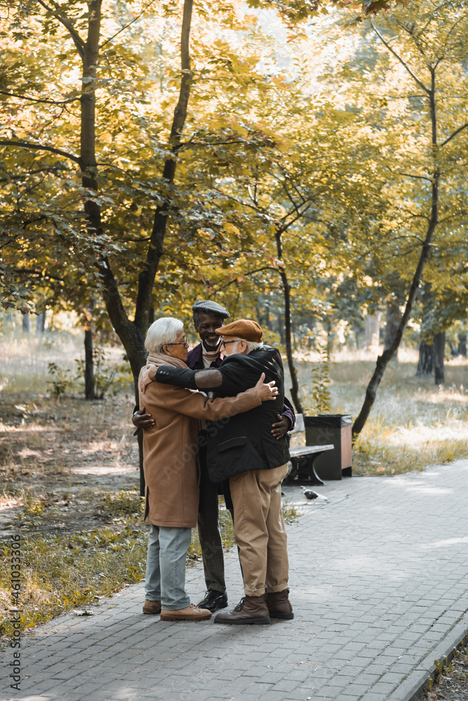 Naklejka premium Positive multicultural friends hugging in autumn park