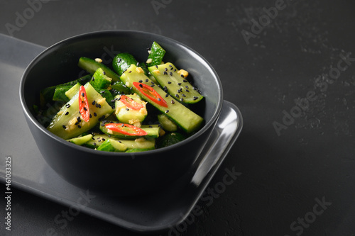 Asian spicy broken Cucumber salad with fresh coriander, ginger, pepper chili, black vinegar on black background. Spicy cucumbers. Popular Chinese appetizer. Close up.