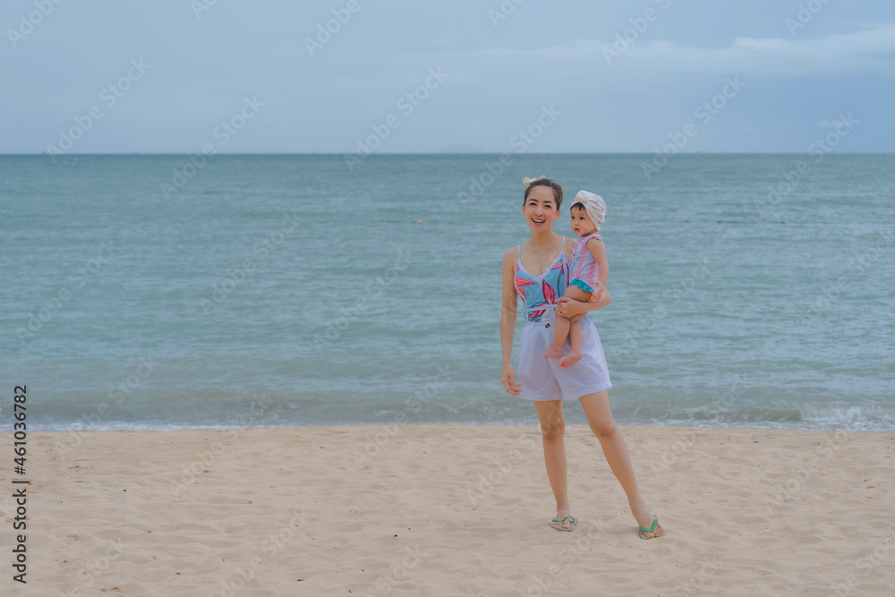 Mother and baby in swimsuit standing happy and relaxing at the beach at the beautiful sea at the evening time. Mother and baby in swimsuit standing happy and relaxing at the beach at the beautiful sea at the evening time.