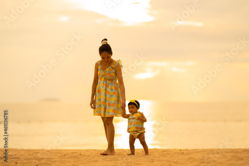 Mother and baby take a walk on the beach with a beautiful sunset.