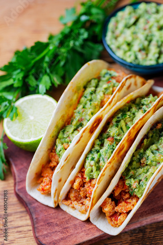 Tacos with fried minced meat and guacamole sauce on a wooden boards. Mexican tacos, cilantro and lime on wooden background. Mexican cuisine. Rustic style