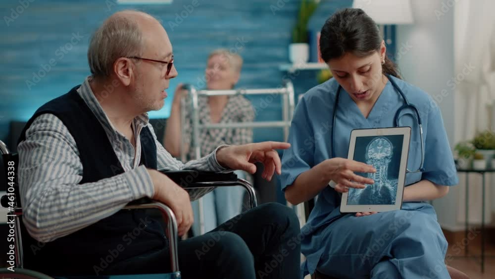 Medical assistant holding tablet with x ray scan for checkup with handicapped man in nursing home. Nurse explaining radiography on digital device to senior patient in wheelchair Medical assistant holding tablet with x ray scan for checkup with handicapped man in nursing home. Nurse explaining radiography on digital device to senior patient in wheelchair