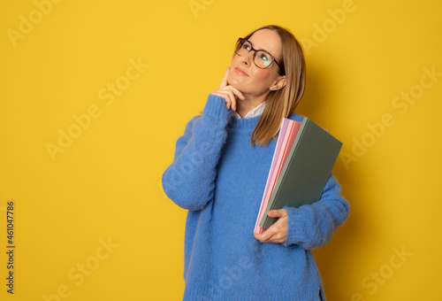Portrait of pensive young caucasian woman holding notebooks isolated on yellow background
