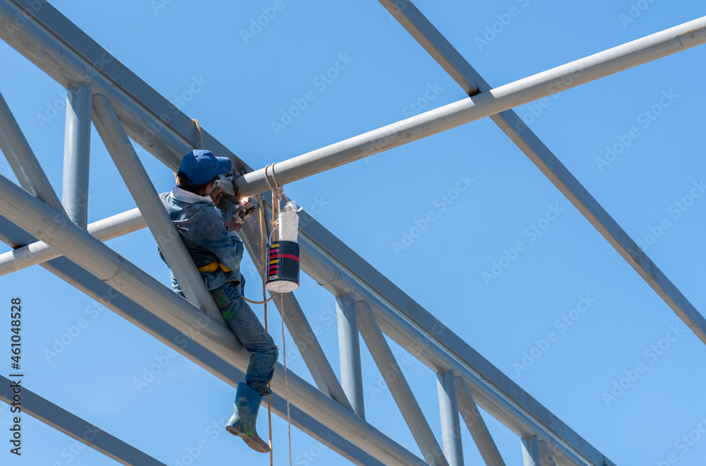 Construction Worker Welding Roof Beam Against Blue Sky.