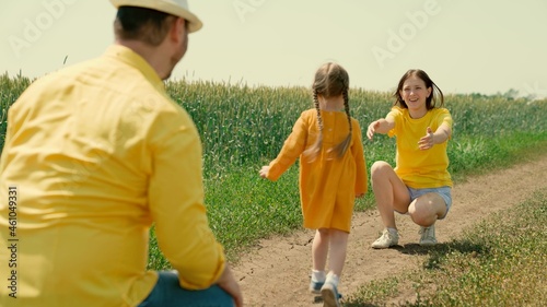 Daughter, girl runs from dad to mom in sun. Happy family plays in wheat field in summer. Father child mother outdoor recreation, family childhood. Weekends with family, children's games with parents