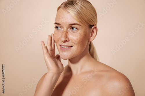 Smiling woman touching her face with finger while standing in studio in front of a pastel background