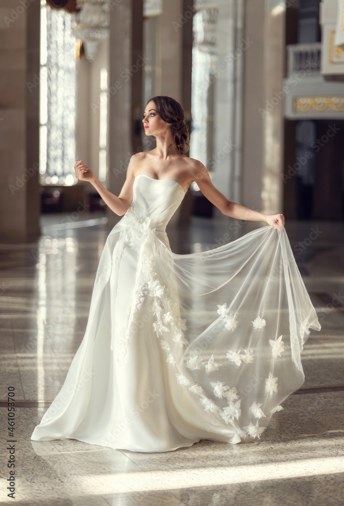 young fragile brunette girl. bride in a luxurious wedding dress in a chic interior with beautiful sunlight from the windows wedding hairstyle and makeup. photo for wedding salt, beauty salon young fragile brunette girl. bride in a luxurious wedding dress in a chic interior with beautiful sunlight from the windows wedding hairstyle and makeup. photo for wedding salt, beauty salon