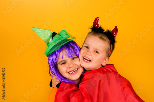 One little toddler boy and girl in a carnival costume for Halloween is isolated on a yellow background. Traditions, holidays concept.