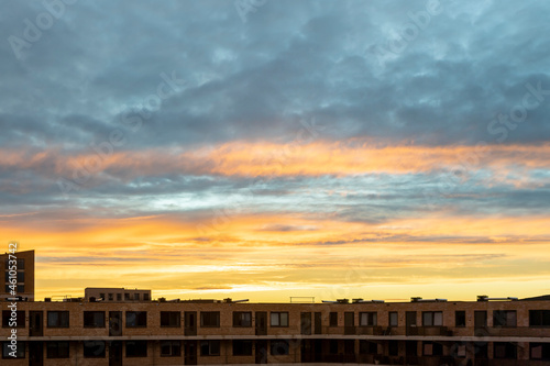 Silhouette contemporary modern exterior facade of apartment building complex lit up orange from the vibrant radiant sunset sky above with textured cumulus clouds