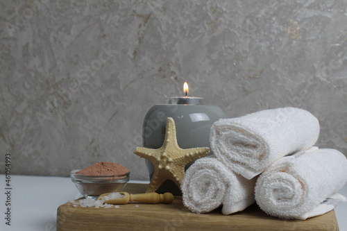 Spa relax massage home body care. White towels oil fragrant for massage aromatherapy candles star sea lie on a wooden tray on a gray background side view