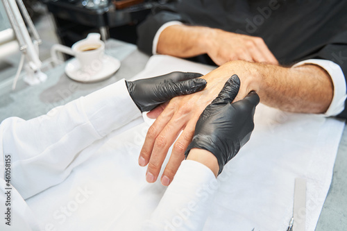 Beautician massaging hand with lotion of Caucasian man
