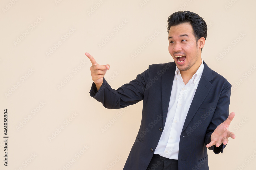 Portrait of surprised Asian businessman wearing suit against plain background Portrait of surprised Asian businessman wearing suit against plain background