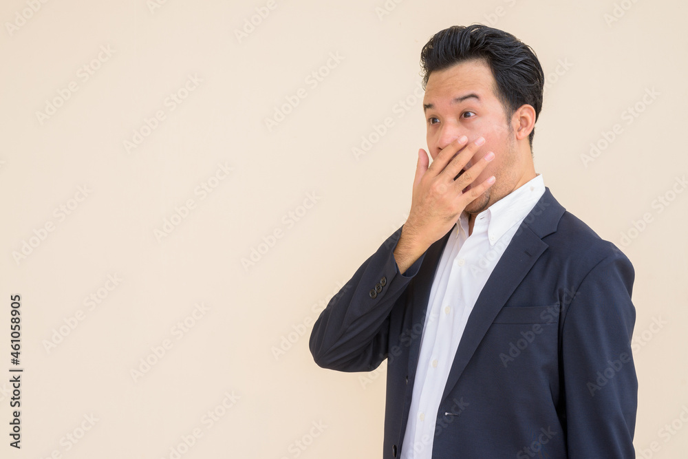 Portrait of Asian businessman wearing suit against plain background while looking shocked Portrait of Asian businessman wearing suit against plain background while looking shocked