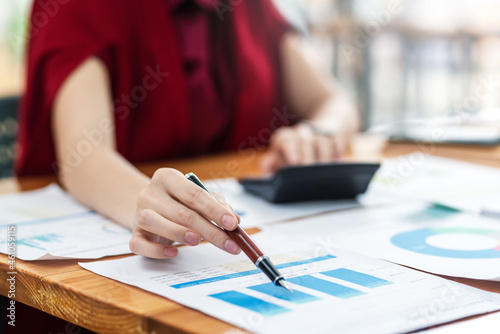 Close-up of a businesswoman hand holding a pen pointing at a graph checking financial analysis at the office.
