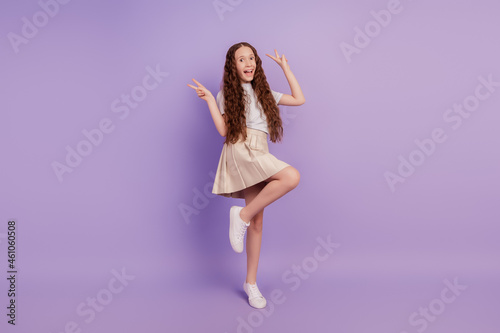 Portrait of cheerful funny nice girl disco dance raise hands show v-signs on purple background