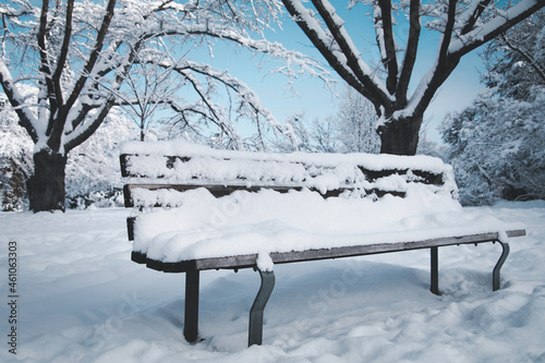 A bench in public park cover with snow and bright sky background in the winter