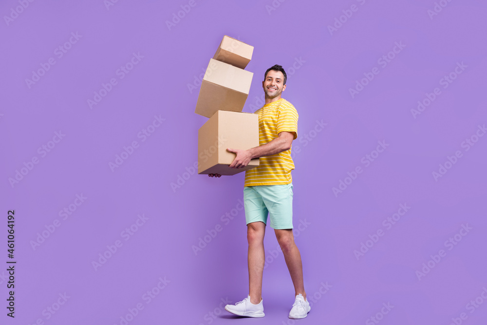Full size profile side photo of young guy happy positive smile hold cardboard delivery isolated over purple color background Full size profile side photo of young guy happy positive smile hold cardboard delivery isolated over purple color background