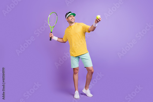 Full body profile side photo of young sporty man happy positive smile play tennis isolated over purple color background
