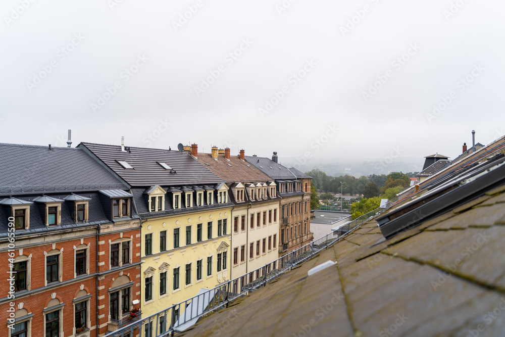 Colorful rooftops of residential buildings with landscape aerial panoramic view to green foggy forest or park on cloudy summer or autumn day. View from window or balcony in Dresden, Germany