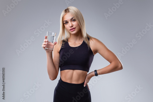 Beautiful sports girl with a glass of water on a gray background. © Aleksandra