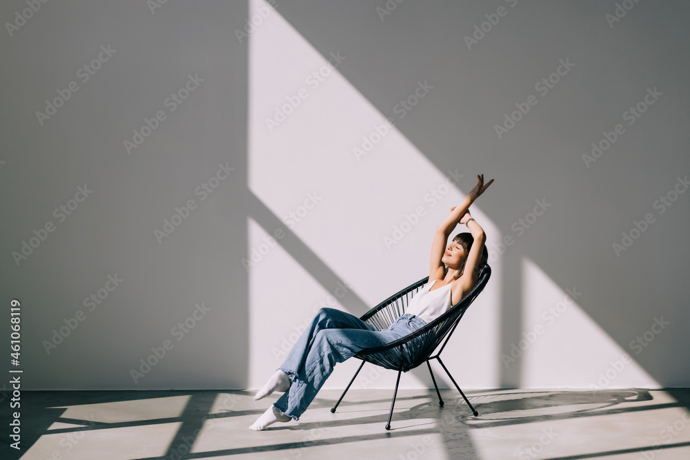 © F8  \ Suport Ukraine - Young woman at home sitting on modern chair in front of window relaxing in her living room
