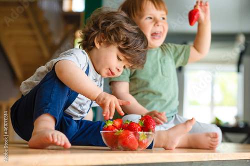 Little brothers eat strawberries are sitting on a wooden table in the kitchen.