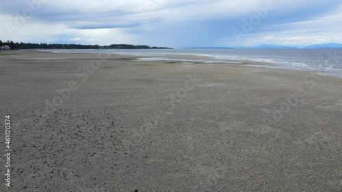 4k aerial view of male person walking along a rocky beach on Vancouver Island, Canada. Camera following from above and behind flying slowly over man and toward ocean. photo