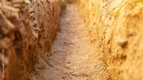 Dig a trench. Earthworks, digging trench. Long earthen trench dug to lay pipe or optical fiber. Construction the sewage and drainage. View from the trench. Clay soil. Part of the image is blurred