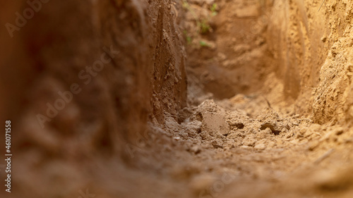 Dig a trench. Earthworks, digging trench. Long earthen trench dug to lay pipe or optical fiber. Construction the sewage and drainage. View from the trench. Clay soil. Part of the image is blurred photo