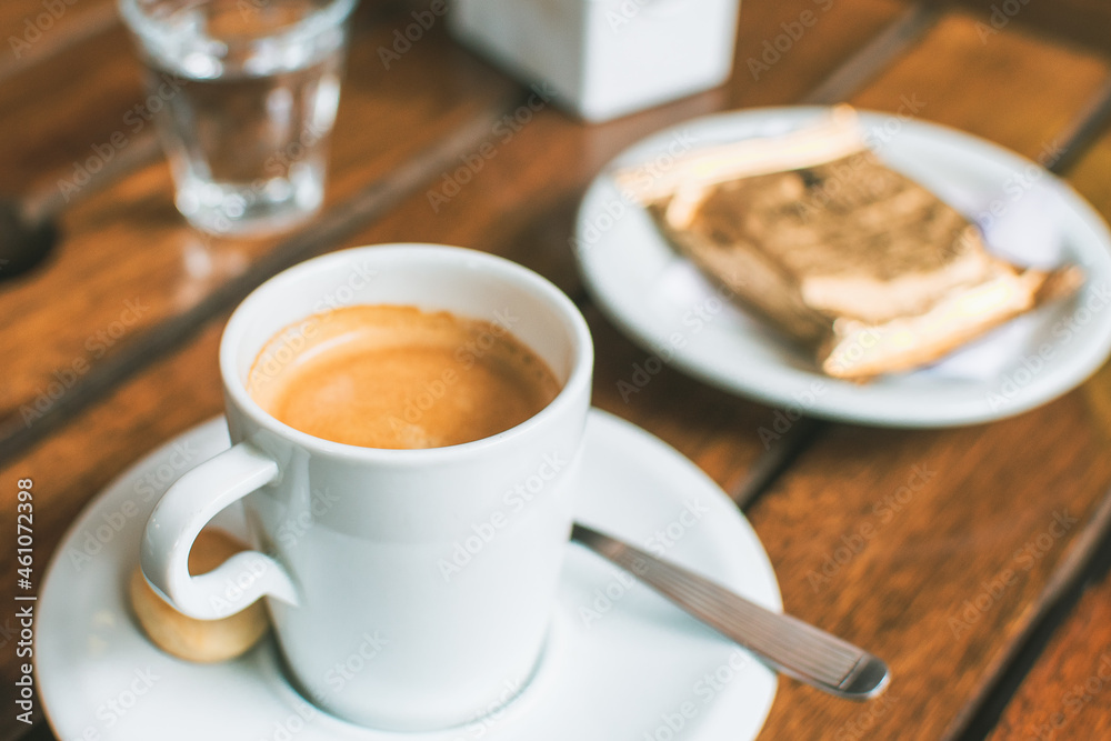 close up to a cup of coffee with a glass of water and a plate with alfajor in the restaurant in the afternoon outdoors