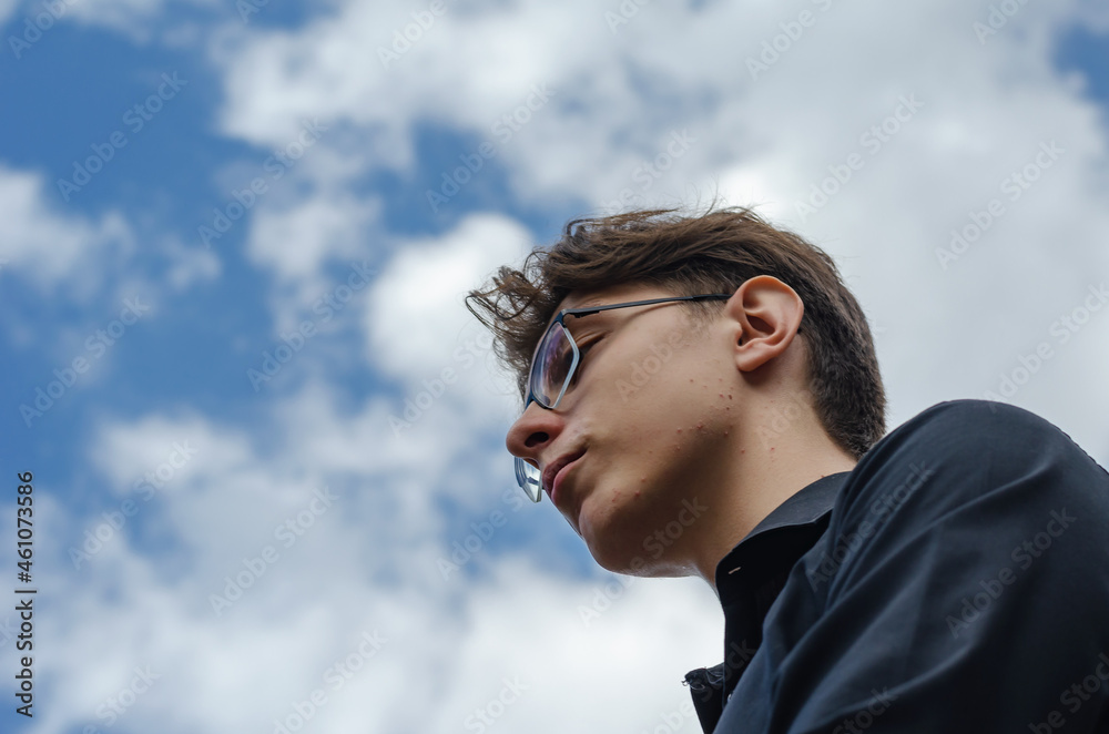 A portrait of a young adult male against a blue sky. A man weari A portrait of a young adult male against a blue sky. A man weari