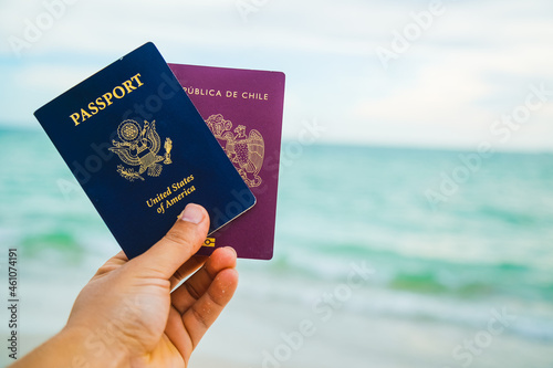 a hand holding two passport a red and a blue one on a beach