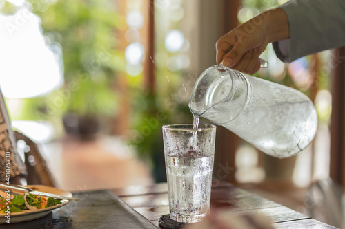 Waiter hand pouring water with ice into glasses on table.