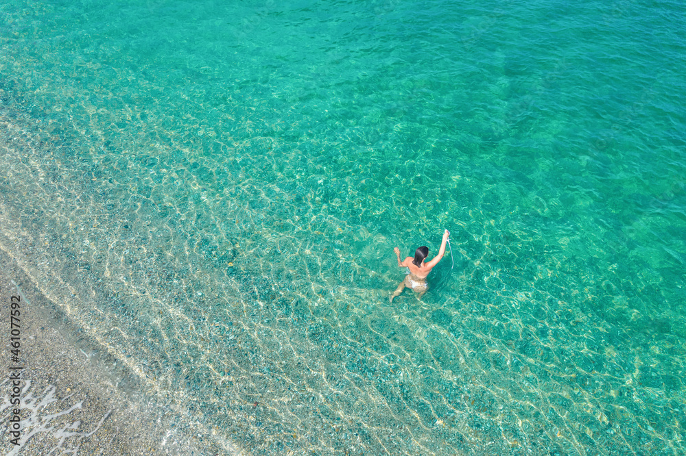 Young nude beautiful, sexy woman with naked breast taking off swimsuit standing in sea, ocean water. Summer. View from above. Top view, copter